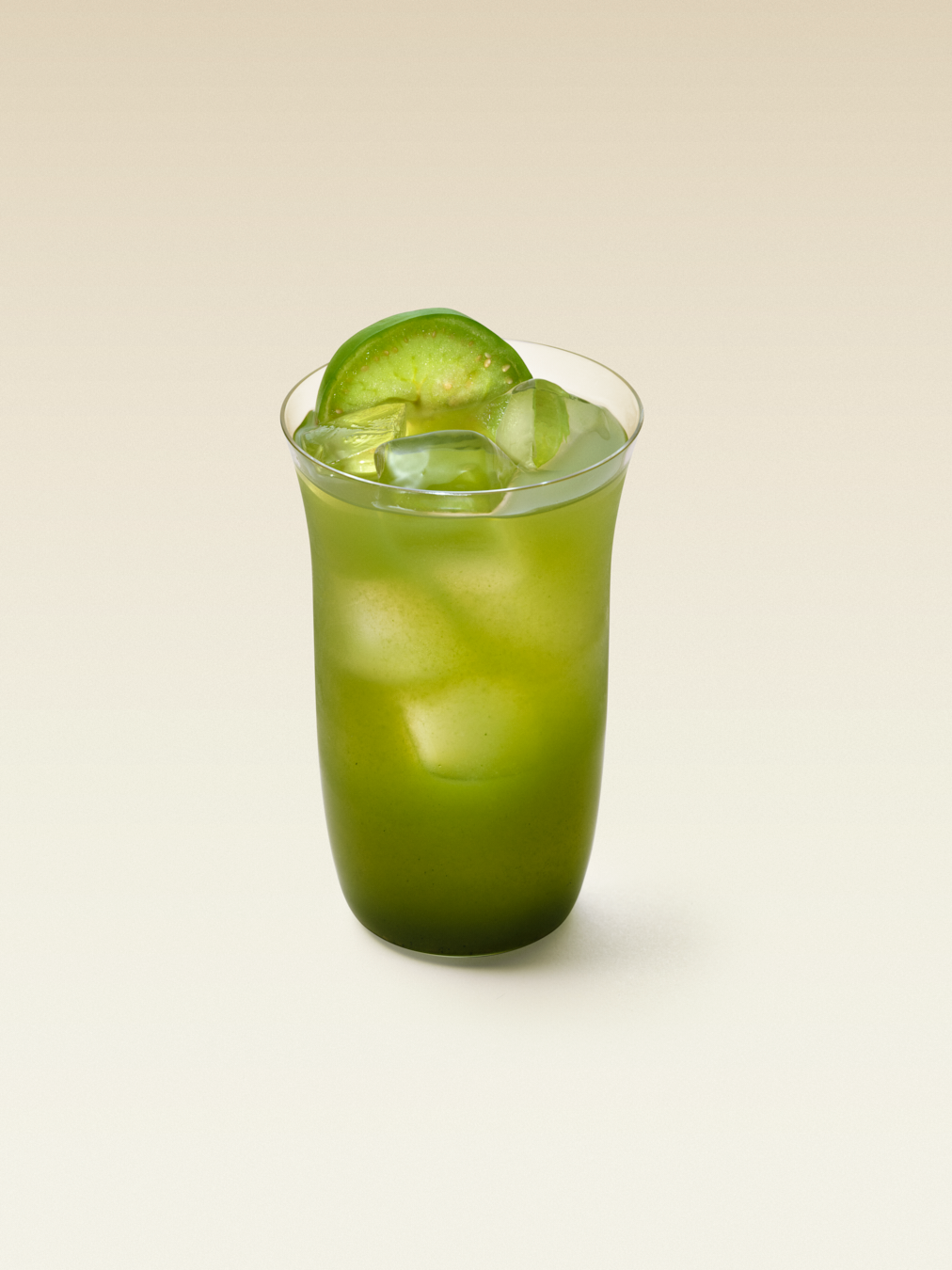 A tall cocktail glass with green liquid and small ice cubes, garnished with a thin slice of green tomato which is called Tomatillo, displaying a green or verde bloody maria cocktail.