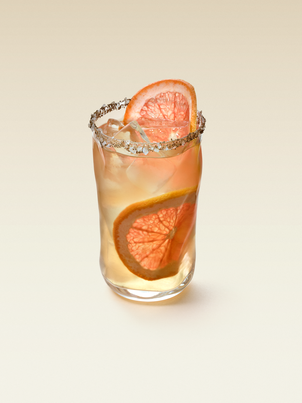 Tall cocktail glass with ice cubes and two slices of grapefruit, displaying a Paloma tequila cocktail.